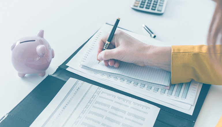 mujer escribiendo en una libreta con una hucha y un papel con numeros que indican si las indemnizaciones tributan o no